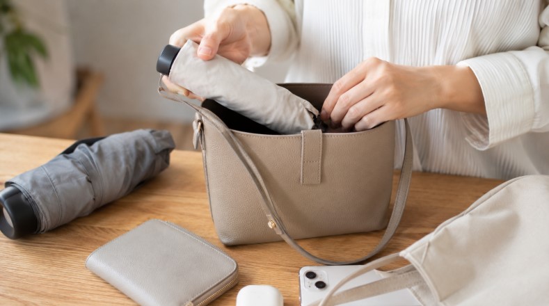 コンパクトな折りたたみ日傘を小さなバッグへ収納する様子